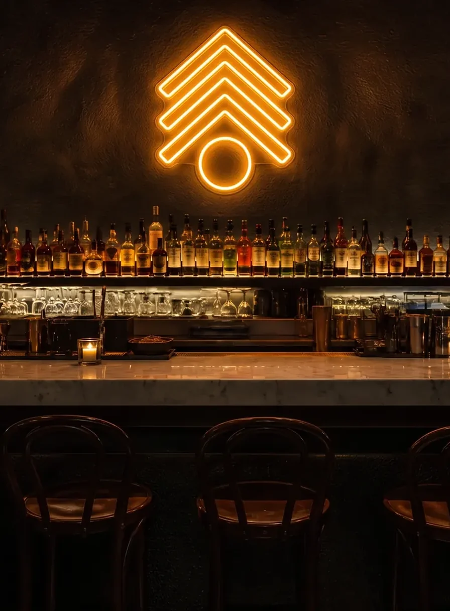 Orange LED neon mark glowing on a dark wall above a lit back-bar shelf of bottles