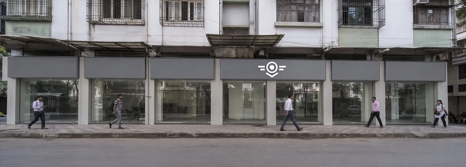 Street-level parade of shopfronts sharing one continuous fascia band, with a fitted sign above the centre unit